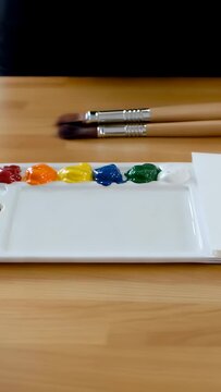 Vertical video: Pulling back camera revealing white palette with six wet dabs and 2 brushes on desk