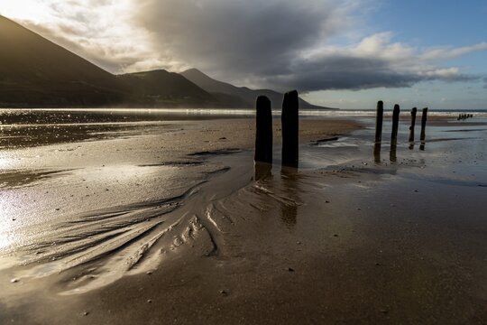 Sandy beach beach with stakes in the sand and mountains and cloudy sky in the background, Killarny, County Kerry, Ireland