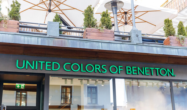 Cortina D Ampezzo, Italy - March 07, 2026: United Colors of Benetton storefront featuring green signage, outdoor seating area with umbrellas and potted plants in a vibrant urban setting