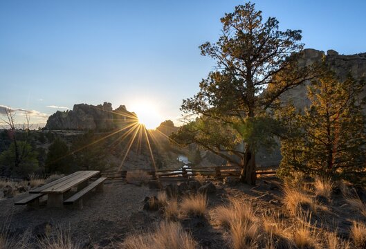 Bench and table at viewpoint, sun star on rock walls, sunset, course of Crooked River, canyon with rock formations, The Red Wall, Smith Rock State Park, Oregon, USA