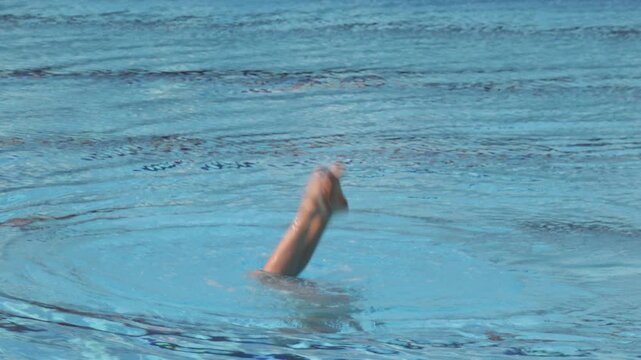 Artistic swimmer performing elegant choreographed leg movements during a synchronized swimming routine in a swimming pool. Sport, grace, flexibility and underwater choreography.