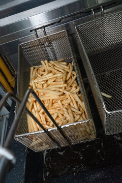 Professional deep fryer basket filled with golden crispy french fries in a commercial restaurant kitchen