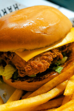 Extreme close up of a crispy fried chicken burger with melted cheese and fresh greens on a toasted bun