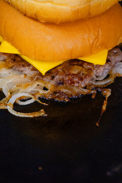 Smashed burger patty cooking with onions and melted cheese on a sizzling hot professional flat top grill