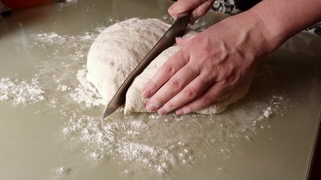 Close-up of hands using a knife to divide and shape raw dough on a floured surface, captured in smooth slow motion