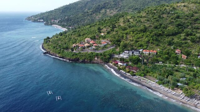 Cinematic aerial drone moving left along black sand shoreline and coastal village in Amed, Bali, Indonesia.