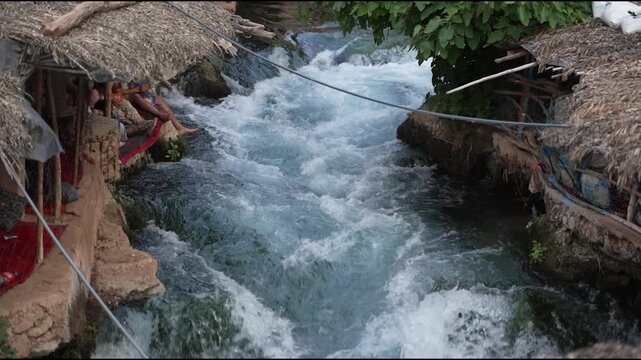 Scenic view of traditional rustic cafes with thatched roofs built over the fast-flowing Oum Er-Rbia river springs in the Middle Atlas mountains, Morocco.