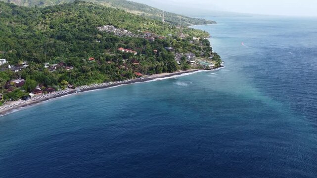 Cinematic aerial drone moving slowly forward from ocean toward coastal village landscape in Amed, Bali, Indonesia.