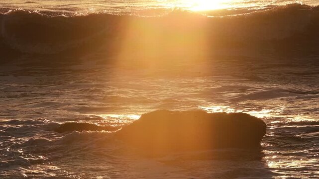 A breaking ocean wave backlit by the sun during sunset. Filmed in Costa da Caparica, Portugal, the visuals highlight nature and the movement of water.