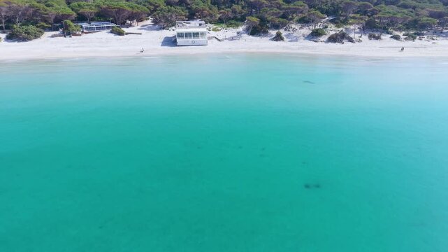 Aerial pull back view of Maria Pia beach in Sardinia showing turquoise clear water sandy shore and coastal landscape on a sunny day