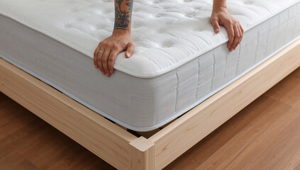 Naklejka premium Close-up of hands touching a new mattress on a wooden bed frame, emphasizing comfort and quality