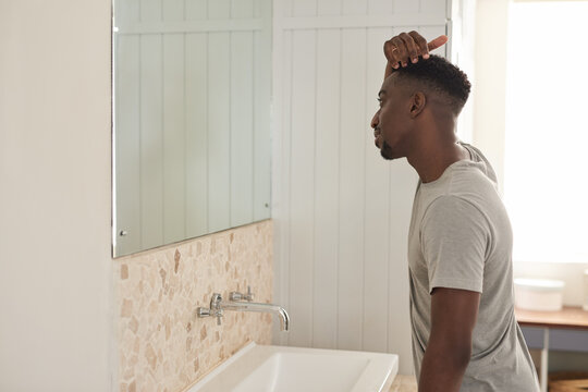 Young African man looking at his hairline in a bathroom mirror