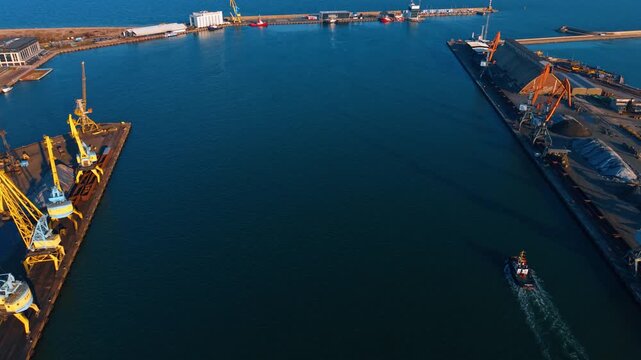 Wide view of sea harbor with tugboat and cranes. Aerial perspective of port entrance, calm water and industrial docks.
