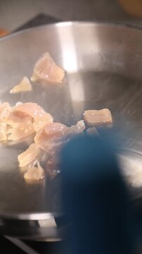 Cocinero profesional con guantes de l&aacute;tex negro fr&iacute;e peque&ntilde;os trozos de grasa de jam&oacute;n ib&eacute;rico en una sart&eacute;n de acero inoxidable, generando un chisporroteo intenso y aromas ricos durante la cocci&oacute;n.