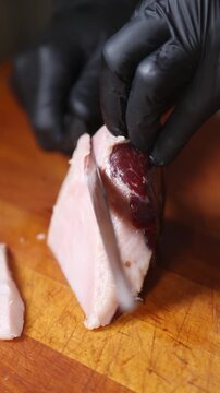 Un cocinero profesional con guantes de l&aacute;tex negro corta finas lonchas de jam&oacute;n ib&eacute;rico de una maza, realizando movimientos precisos con el cuchillo sobre una tabla de cortar de madera.
