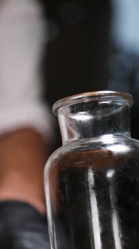 Un cocinero profesional con guantes de l&aacute;tex negro introduce trozos de melocot&oacute;n y tiras de piel de naranja en un bote de cristal transparente, preparando los ingredientes para elaborar un alm&iacute;bar