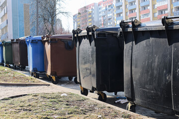 Row of large garbage containers and recycling bins on urban sidewalk near apartment buildings....
