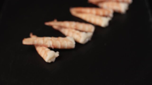 Freshly cooked peeled prawns arranged neatly in a row on a sleek black background, an ideal ingredient for seafood appetizers, salads, and healthy gourmet recipes