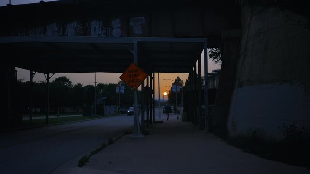 Urban street view through a bridge silhouette at sunset with construction sign