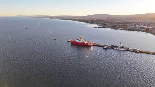 Aerial circling the iconic red polar research ship RRS Sir David Attenborough as it sits docked at Prat Pier in Punta Arenas, Chile, during a golden Patagonian