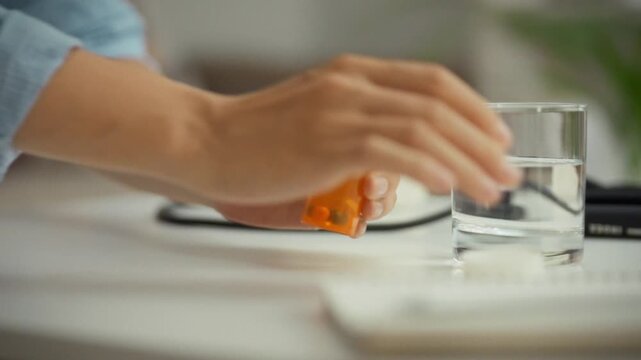 A woman follows her daily health regimen by carefully opening an orange prescription bottle, removing pills for her vitamin treatment as part of her ongoing patient care and self-medication routine