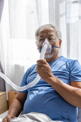 Senior Asian man wearing oxygen mask breathing with difficulty feeling tired sick patient resting...