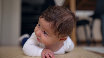 Fototapeta premium Baby lying on belly, head slightly tilted, observing surroundings with curiosity, early childhood exploration, gentle smile, home setting, candid and natural