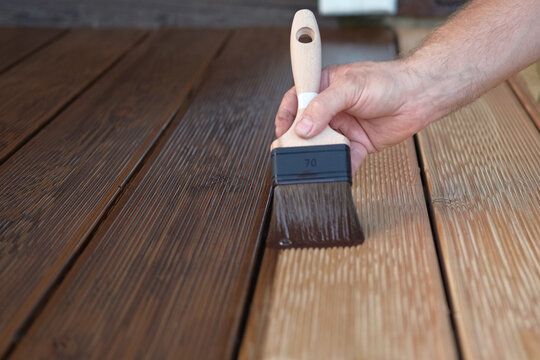 Brown oil for protection of wood by staining. Painting a larch for protecting and pests. Woodworker applying finish to terrace deck board. Repairman varnishing with brush wooden plank floor surface.