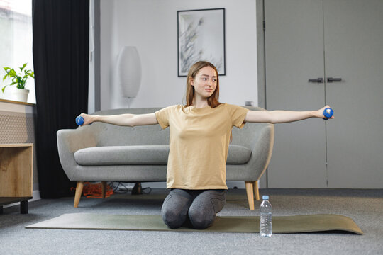 Portrait of young woman excercising with dumbbells at home on a mat