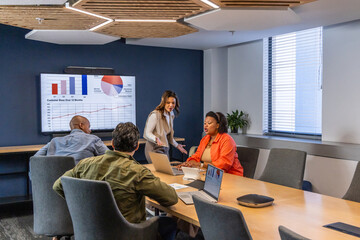 Obraz premium Diverse coworkers presenting charts on wall display in meeting room in office attire using laptops