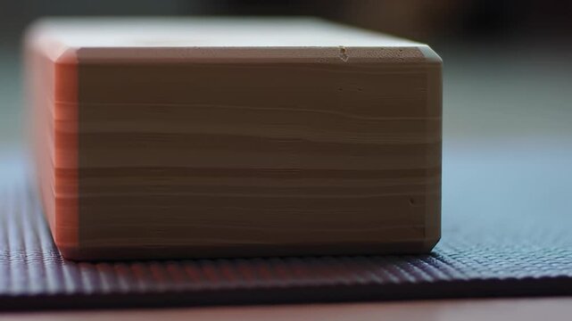 Close-up of a wooden yoga block resting on a textured dark purple yoga mat