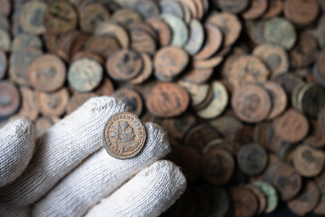 Gloved hand holding an ancient Roman coin. Close up of bronze emperor portrait coin from a treasure hoard. Archaeology and numismatics concept © scaliger