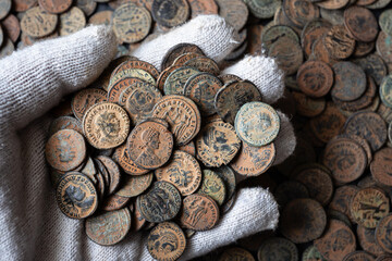 Hand in white glove holding ancient Roman coins. Archaeological discovery of a bronze coin hoard. Numismatics and historical money concept © scaliger