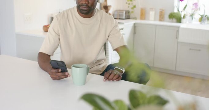 Smartphone pinging, man checking it at counter, putting on headphones, smiling at message with mug