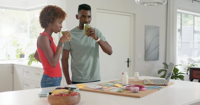 Diverse couple sipping green drinks at kitchen island, reviewing cork board samples and planning