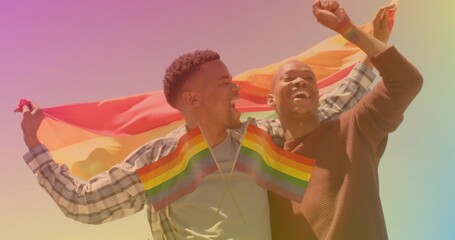 Holding pride flag, couple wearing plaid and brown sweater in field with crossed flags at chest