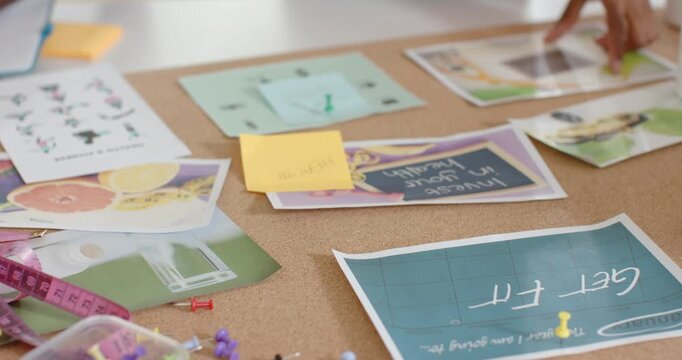 African American team arranging corkboard on table for planning, smoothing prints and pinning notes