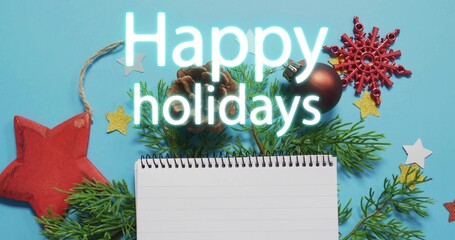 Displaying spiral notebook centered on blue surface with pine sprigs, pinecone, Happy holidays text