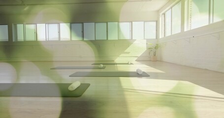 Displaying empty yoga studio featuring dark mats on wood floor, featuring windows and rolled towels