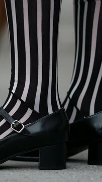 Vertical video: Shifting wearer in striped tights adjusting Mary Jane shoes on ground steadying