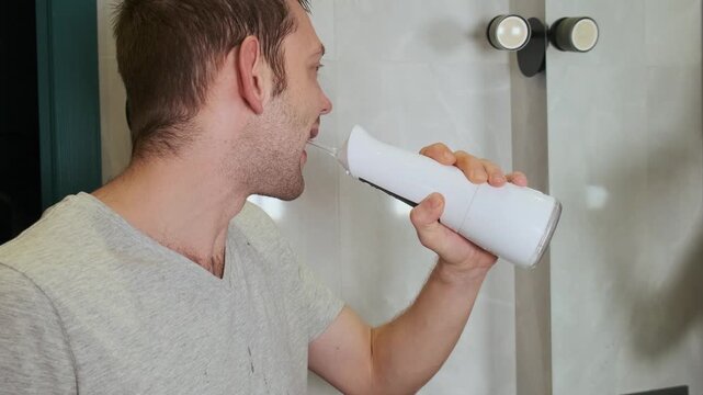 Man using electric water flosser for dental hygiene in bathroom. Daily hygiene routine and morning self care. Oral health and dental care. Personal health habits and simple routine of starting the day