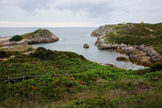 Rocky coast with green cliffs and a small bay under a cloudy sky