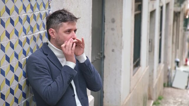 A man stands outdoors in Lisbon, Portugal, playing the harmonica. He shares his music on a busy city street as passersby enjoy the performance.