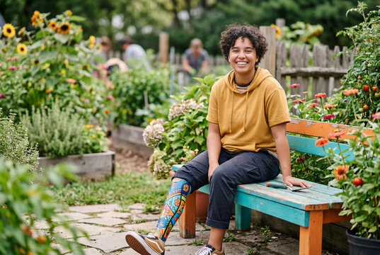 Joyful adult with a colorful prosthetic leg sitting on a wooden bench in a lush community garden