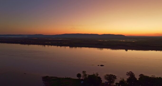 A breathtaking aerial view of sunset casting golden light over the Nam Kading River and Pak Kading Bridge, creating vivid reflections and a peaceful evening atmosphere in central Laos.