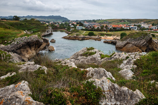 Rocky Bay with Coastal Village and Green Cliffs Under a Cloudy Sky