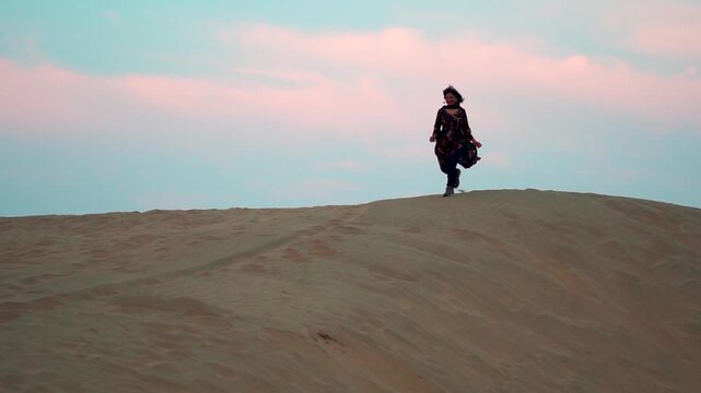 Silhouette shot of Indian teenage woman running on dune during sunrise in desert at Jaisalmer, Rajasthan, India. Tourist wearing traditional Indian salwar suit end enjoying vacation. 