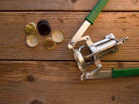 Close up of some crown corks and a manual crown capper on a wooden table.