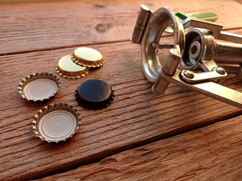Close up of some crown caps and a manual crown capper on a wooden table.