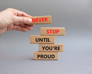 Never Stop symbol. Wooden blocks with words Never Stop Until You are Proud. Businessman hand. Beautiful grey background. Business and Never Stop concept. Copy space